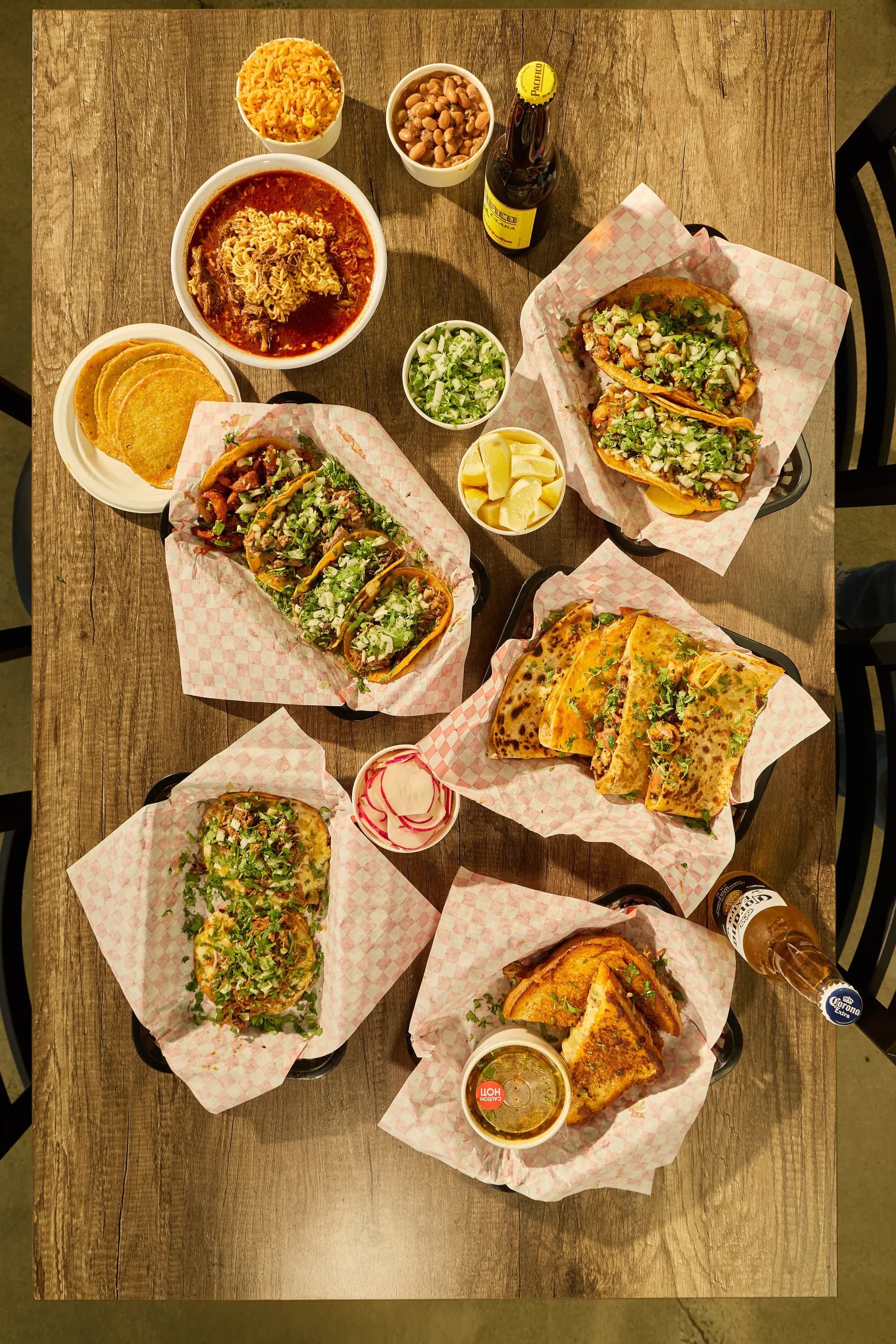 Overhead spread of Mr. Birria tacos, quesadillas, birria ramen and sides — platter-style Mexican food