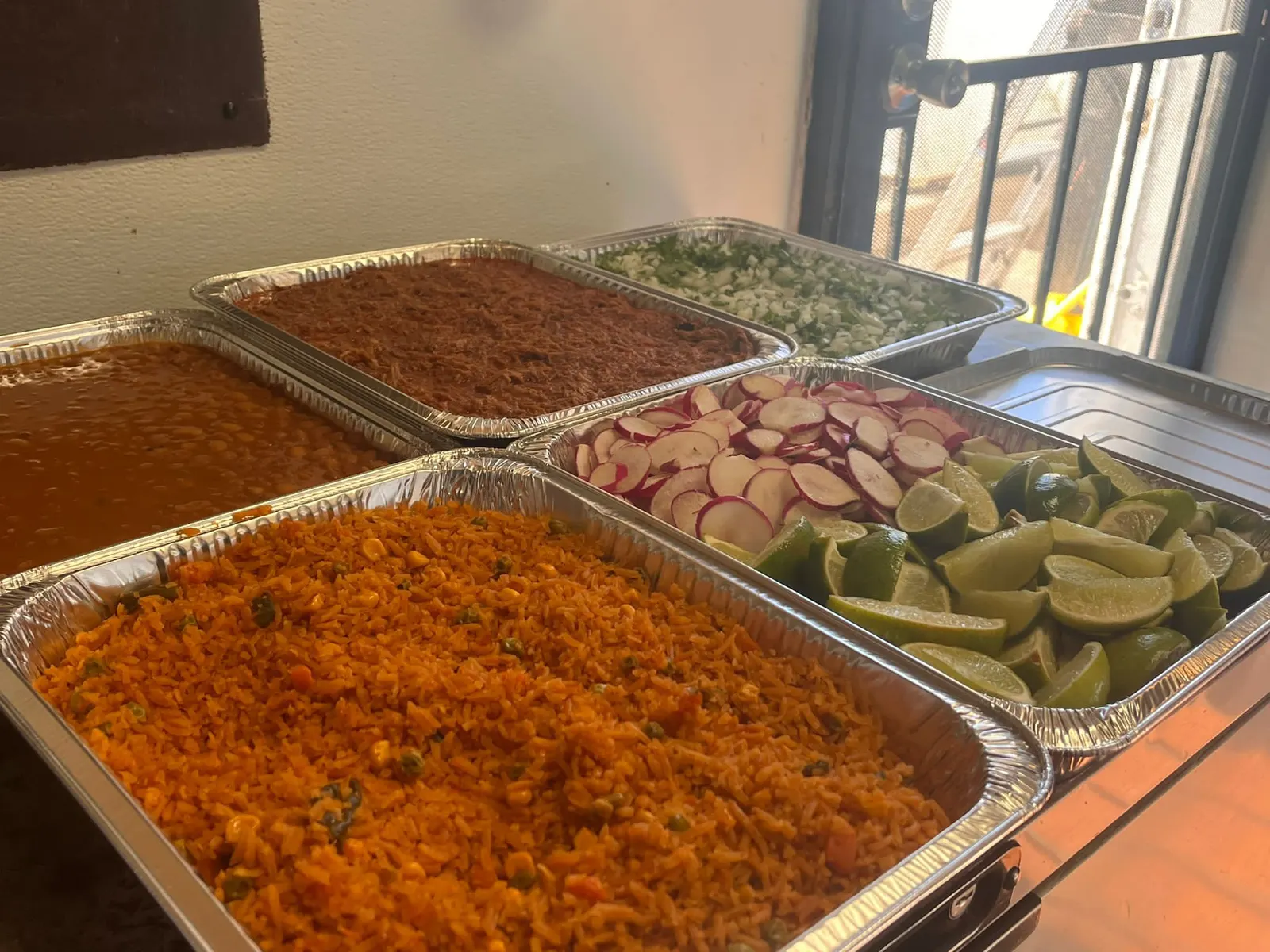 Mr. Birria catering platter spread: trays of birria, rice, beans, limes and garnishes